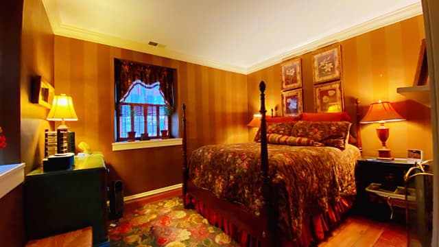 Pierpoint Suite: Warm-toned bedroom with floral-patterned bedspread, two matching lamps, and striped walls. Cozy and inviting atmosphere with a vintage touch.