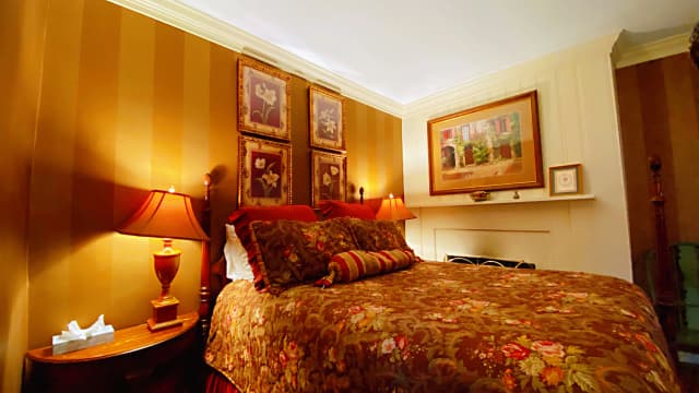 Pierpoint Suite: a bedroom featuring warm, muted lighting, an ornate floral bedspread, vintage floral artwork, and elegant lamps on either side of the bed.